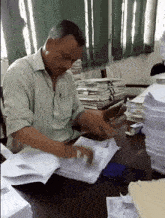 a man sits at a desk surrounded by stacks of papers including one that says ' a ' on it