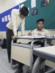a man standing next to a boy sitting at a desk