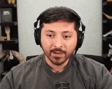 a man with a beard wearing headphones and a gray shirt with the letter h on it