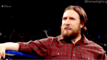 a man with a beard wearing a plaid shirt is talking to another man in a ring .
