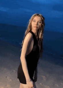 a woman in a black dress is standing on a sandy beach