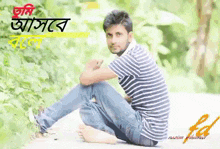 a man in a striped shirt sits barefoot in front of a green background