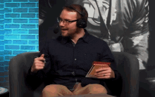 a man wearing headphones and glasses holds a notebook