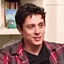 a young man in a plaid shirt and black shirt is sitting on a couch .