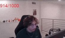 a man is sitting in a chair in front of a computer screen with the number 914/1000 written on the wall behind him .