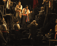 a group of men are standing on a stage and one of them has a red scarf around his neck