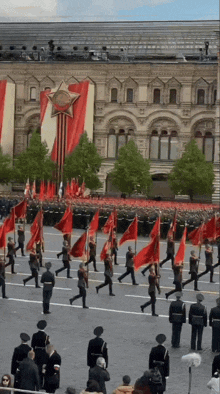 a group of people marching with red flags in front of a building with a star on top