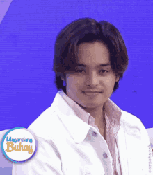 a young man wearing a white jacket is smiling in front of a sign that says ' laging buhay '