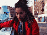 a woman in a red jacket is standing in front of a building looking down