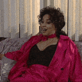 a woman is sitting on a couch wearing a pink coat
