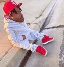 a man wearing a red hat and white pants is sitting on the sidewalk .