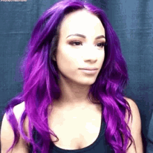 a woman with long purple hair is wearing a black tank top and looking at the camera .