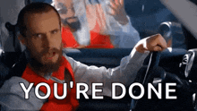 a man with a beard is driving a car and the words `` you 're done '' are behind him .