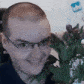 a man wearing glasses is sitting in front of a vase of flowers and smiling .