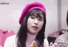 a woman wearing a pink beret and a white sweater is eating a sandwich .