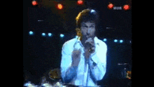 a man is singing into a microphone in a dark room with lights behind him .