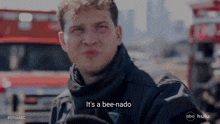 a man in a black jacket says it 's a bee-nado in front of a fire truck