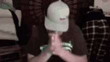 a man wearing a white hat and a brown shirt is sitting in a room with his hands folded in prayer .