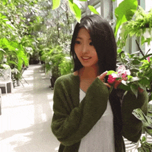 a woman in a green cardigan holds a pink flower