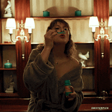 a woman in a bathrobe blowing soap bubbles in a bathroom