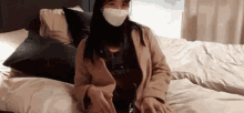 a woman wearing a mask is sitting on a bed with headphones on .