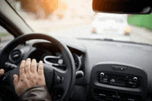 a person is driving a car on a city street and their hand is on the steering wheel .