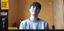 a young man wearing headphones is smiling in front of a yellow sign that says nagy szin pad