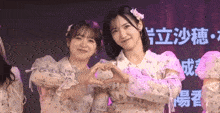 two girls are making a heart shape with their hands in front of chinese characters