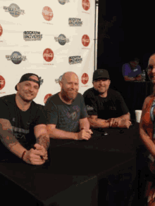 a group of men sitting at a table in front of a banner that says rock the universe
