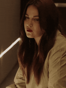 a woman with long red hair is wearing a tan shirt and red lipstick
