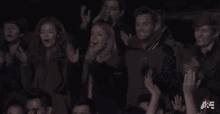 a group of people applauding in a dark room with the letters a & e on the bottom