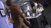 a man in a red shirt walks past a desk with a name tag that says ' sgt. scott '