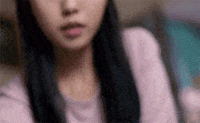 a close up of a woman 's face with long black hair and a pink shirt .