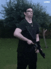 a man in a black shirt holds a rifle in front of trees and a luma logo