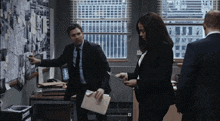 a man in a suit is pointing at a bulletin board while a woman holds a clipboard