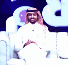 a man in a white shirt and red and white head scarf is sitting on a couch