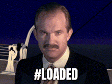 a man with a mustache is standing in front of a ship and the words #loaded are displayed above him
