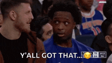 a man in a blue shirt is talking to another man in a crowd while a basketball game is being played .
