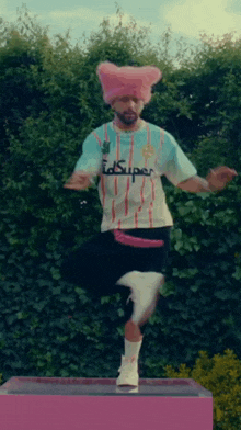 a man wearing a pink hat and a shirt that says id super is standing on one leg