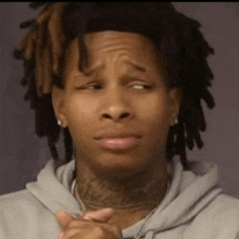 a man with dreadlocks and a tattoo on his neck is making a sad face