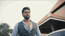 a man with a beard and a vest is standing in front of a building .