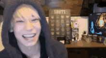 a man is smiling in front of a shots sign