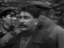 a man with a mustache is standing in front of a brick wall with two other men .