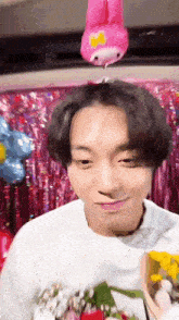 a young man is holding a bouquet of flowers in front of a pink balloon on his head .