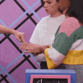 a woman in a colorful sweater is holding another woman 's hand and pointing at it .