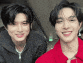 two young men are posing for a picture together and one is wearing a red jacket