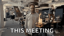 a man is holding a piece of wood that is on fire and the words this meeting are behind him .