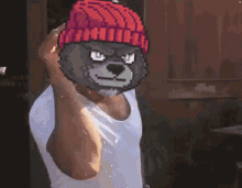 a man wearing a white tank top and a red beanie with a pixelated bear on his face .