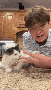 a young man is petting a cat while a black cat sits on the cabinets
