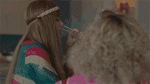 a woman wearing a braided headband sits next to another woman with curly hair